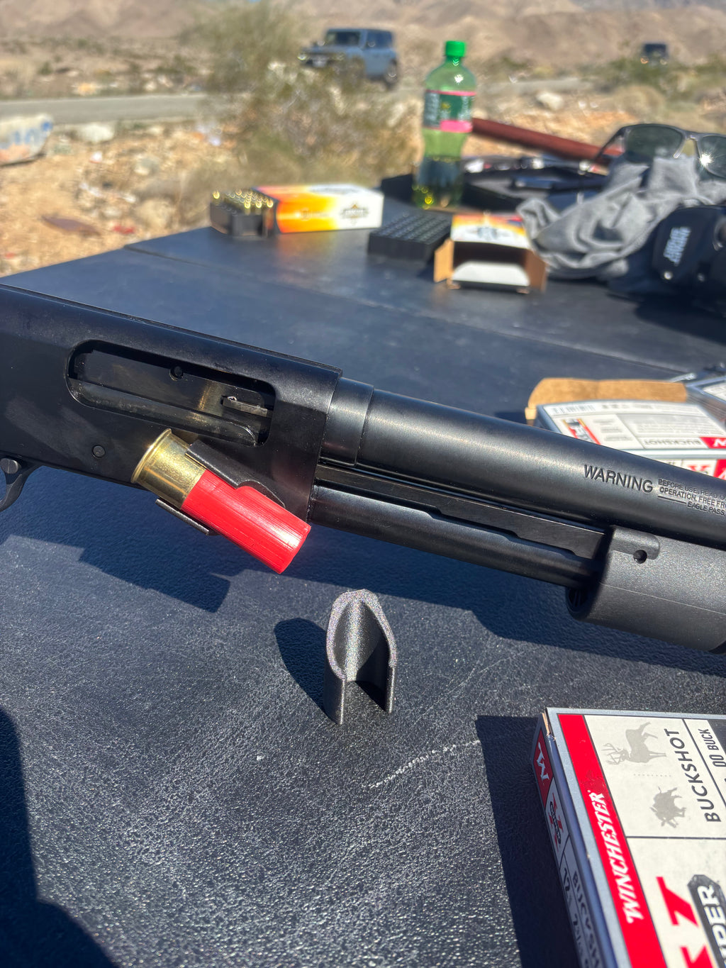 Black shotgun with shell and ammunition on a vehicle's open lid, desert landscape in the background