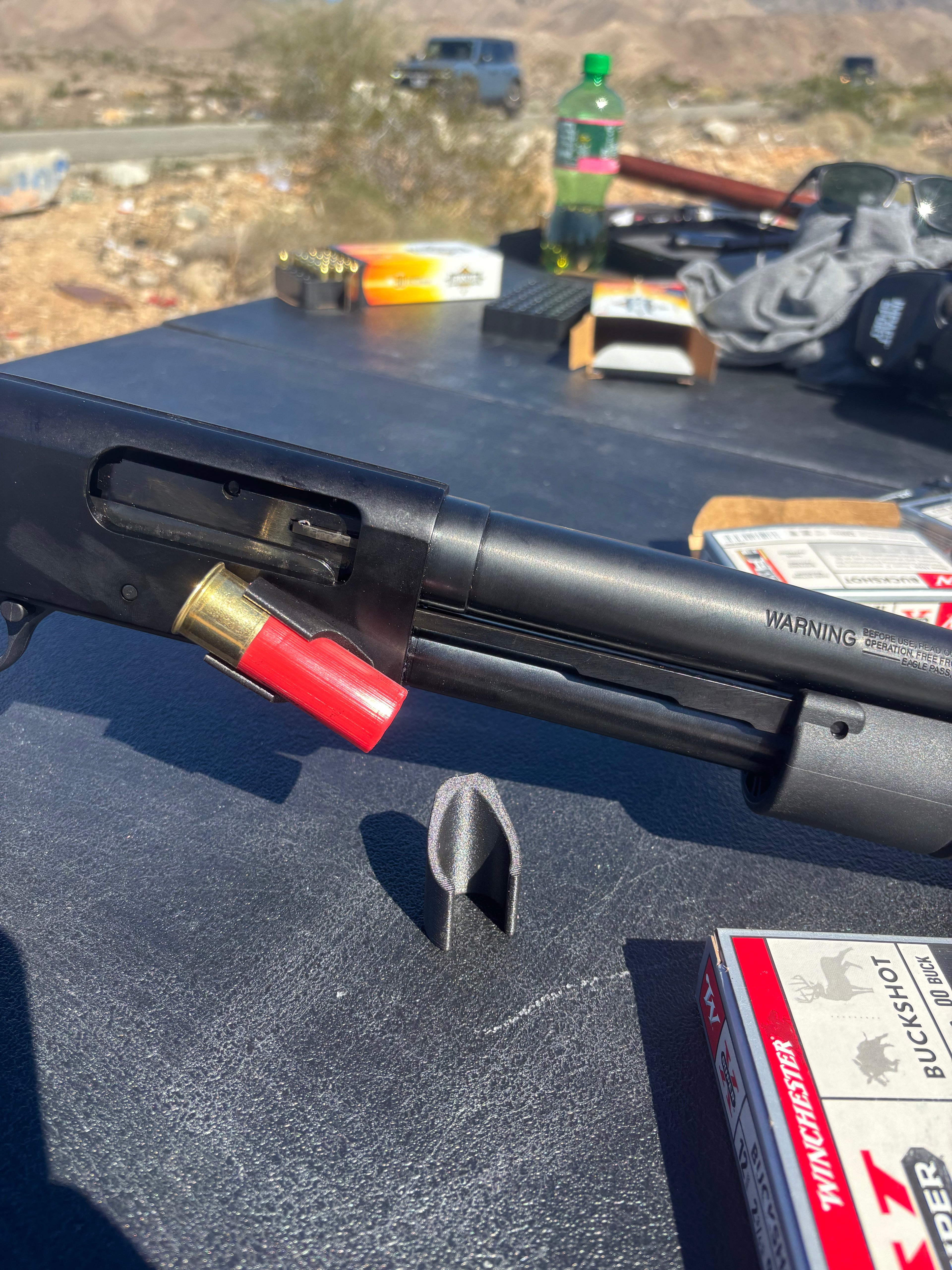 Black shotgun with shell and ammunition on a vehicle's open lid, desert landscape in the background